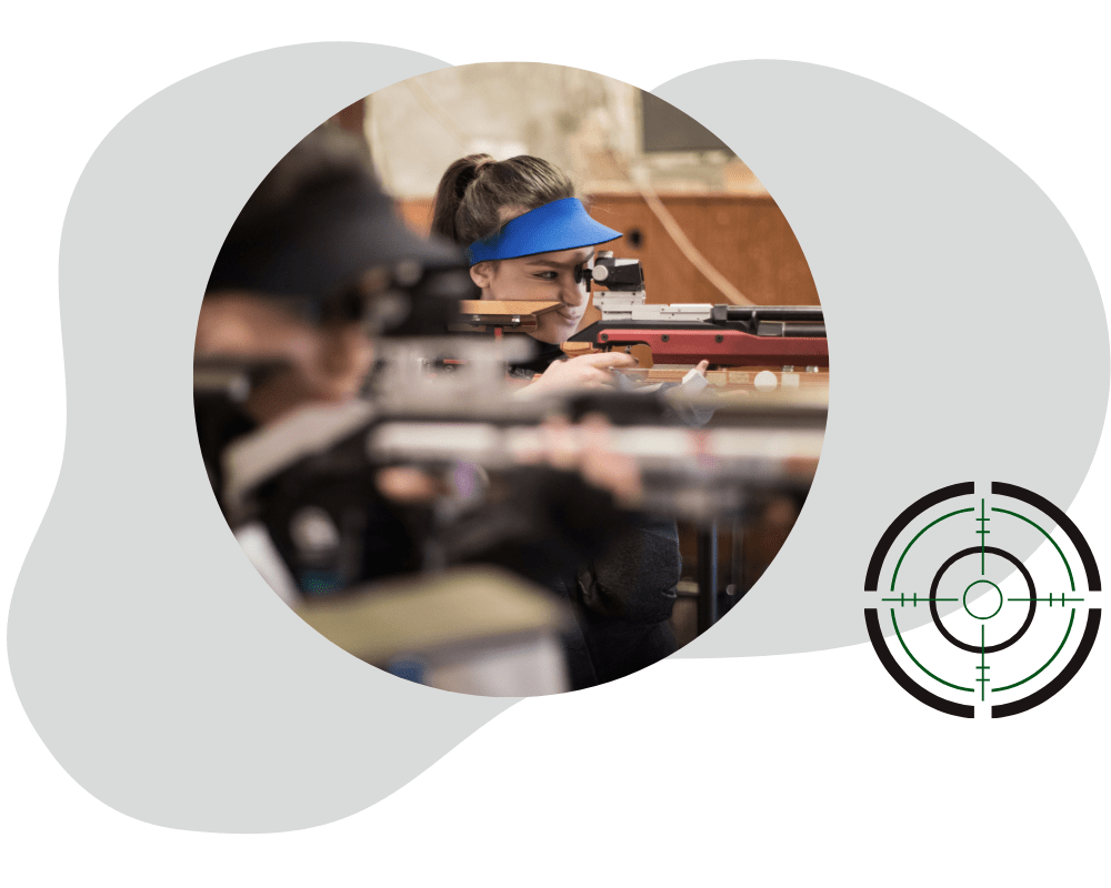 Frau zielt mit einem modernen Luftgewehr auf eine Schießscheibe in einer Schießhalle. Im Vordergrund ist ein stilisiertes Fadenkreuz-Logo zu sehen.